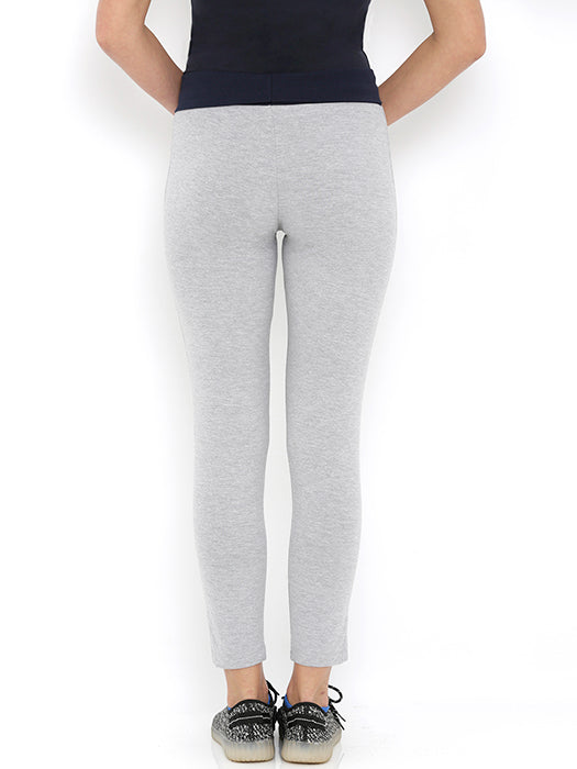 Person wearing narrow fit track pants in light gray with a black top and black sneakers, standing against a white background, back view—an outfit designed for supreme comfort.