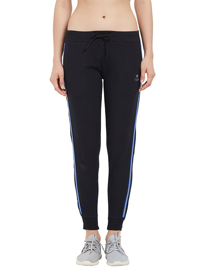 A woman wears Classic Joggers TLC02SS in black with blue side stripes and a drawstring closure, paired with gray sneakers against a white background—ideal for upgrading your casual wardrobe.