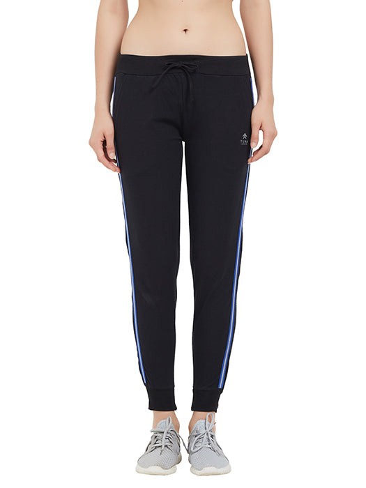 A woman wears Classic Joggers TLC02SS in black with blue side stripes and a drawstring closure, paired with gray sneakers against a white background—ideal for upgrading your casual wardrobe.