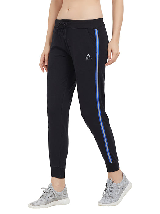 A person wearing Classic Joggers TLC02SS—black with blue stripes, drawstring closure—and gray sneakers, standing against a white background.