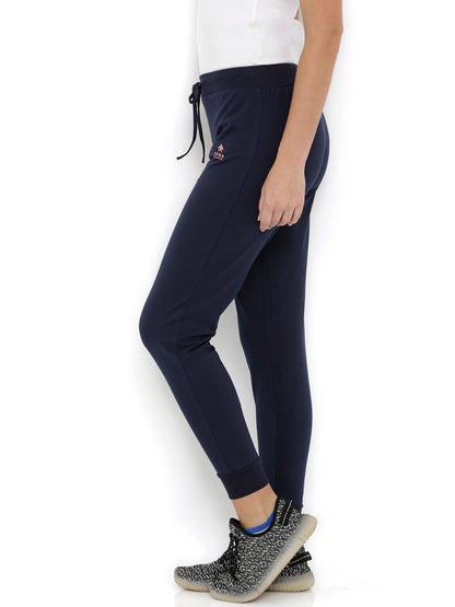 A woman stands sideways in Blue Classic Joggers TLC04 with an adjustable fit, paired with a white top and black sneakers—ideal lounge wear for effortless comfort.